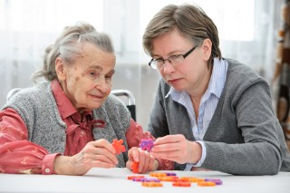 Foto zum Projekt ANKER; Pflegekrankenschwester, die Puzzle mit älterer Frau im Pflegeheim spielt